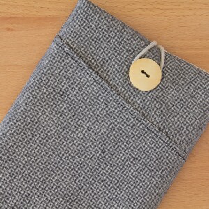 May include: A gray fabric pouch with a small wooden button closure. The pouch is made of a textured fabric with a subtle pattern.