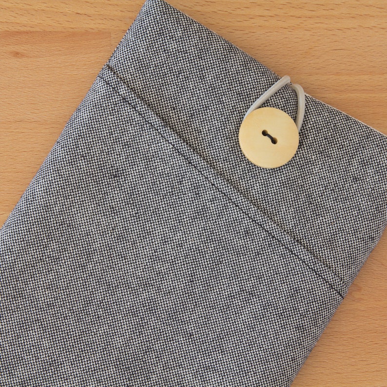 May include: A gray fabric pouch with a small wooden button closure. The pouch is made of a textured fabric with a subtle pattern.