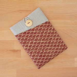 Op de afbeelding: Een tablet hoes van beige linnen en rode stof met een decoratief patroon van rode golven op een beige achtergrond. Een houten knoop is bevestigd aan de hoes.