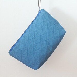 May include: A blue quilted zippered pouch hanging from a metal hook. The pouch is made of a soft, textured fabric.