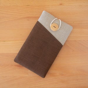 May include: A rectangular tablet sleeve in brown and beige fabric. The sleeve has a diagonal colour block design with a brown lower section and a beige upper section. A wooden button and elastic loop secure the sleeve.