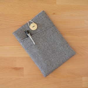 May include: A gray fabric pouch with a zipper closure and a wooden button. A black pen and a silver hair clip are inside the pouch.