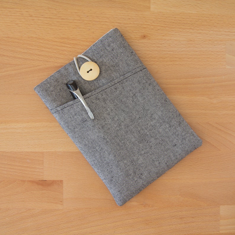 May include: A gray fabric pouch with a zipper closure and a wooden button. A black pen and a silver hair clip are inside the pouch.