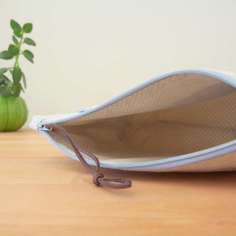 May include: A light blue zippered pouch with a brown drawstring closure. The pouch is lined with a white fabric with a subtle dotted pattern.