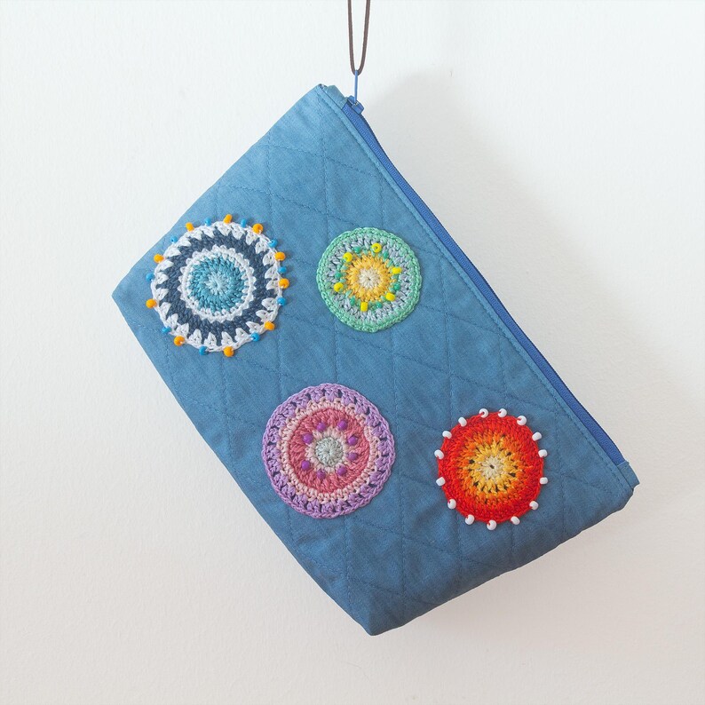 May include: A blue denim zippered pouch with colourful crocheted circles decorated with beads. The pouch is quilted and has a diamond pattern.