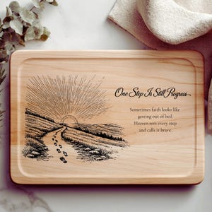 May include: A rectangular wooden serving tray with a light wood grain. The tray features an engraved design of a path leading to a sunrise, with the text "One Step Is Still Progress" and inspirational quotes.