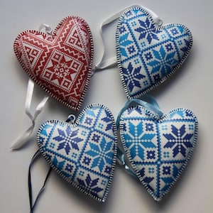 May include: Four heart-shaped ornaments with embroidered patterns. One is red with white accents, and the other three are blue and white. Each has a ribbon for hanging. The ornaments are approximately 10 cm wide.