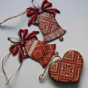 May include: Three wooden Christmas decorations: two bells and a heart. The bells have red bows and red and white patterned designs. The heart-shaped ornament also features the same pattern. All have twine for hanging.