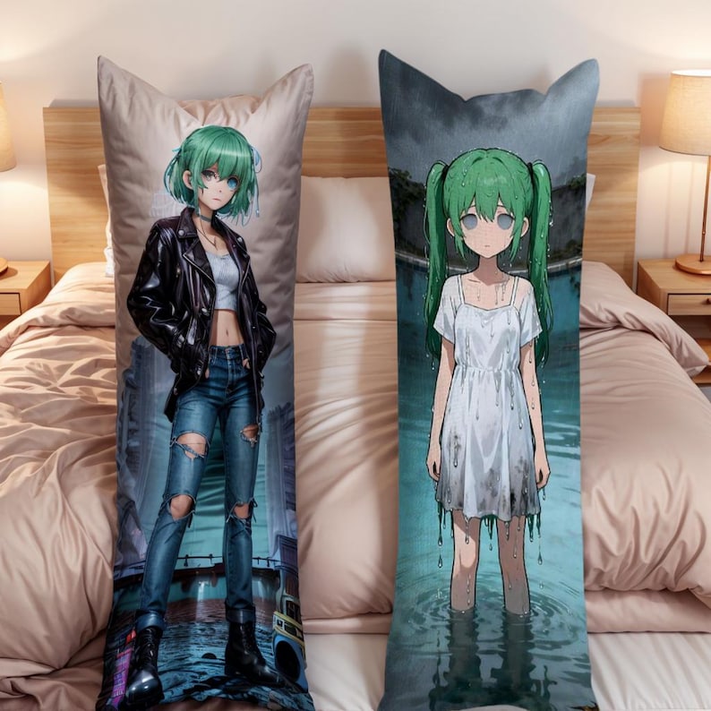 Op de afbeelding: Twee lange lichaamskussens met illustraties in anime-stijl. E&eacute;n toont een vrouw in een zwarte leren jas en een gescheurde jeans. De andere toont een meisje in een witte jurk dat in het water staat. Beide hebben groen haar en een kattenoorvormige top.