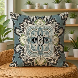 May include: A square throw pillow featuring a symmetrical damask-inspired pattern in shades of dusty blue, sage green, cream, and black. The center of the pillow displays a black monogram with the letters MRP in a decorative, angular font style.