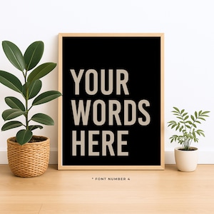 May include: A rectangular wall art print in a light wood frame featuring a black background with the beige text "YOUR WORDS HERE" in a bold sans-serif font. Below the frame, the small text "* FONT NUMBER 4" is printed on the surface.