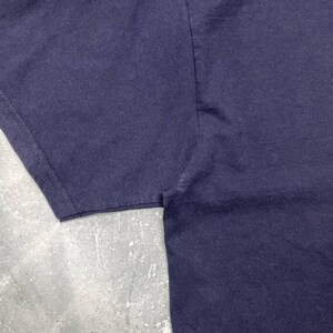 K&ouml;nnte beinhalten: Nahaufnahme eines marineblauen T-Shirts, das die Stoffstruktur und die Nahtdetails am &Auml;rmel zeigt. Das Bild hebt die Verarbeitung und die Farbe des Kleidungsst&uuml;cks hervor.