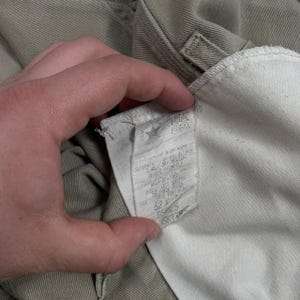 May include: Close-up of khaki-colored pants with a white interior lining. A tag with washing instructions and size information is visible. The tag indicates a size 32 waist.
