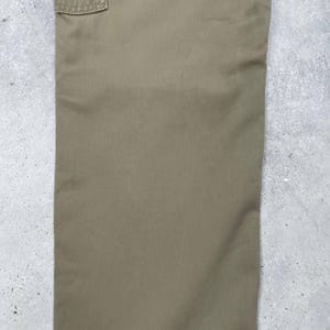 May include: Close-up of khaki-colored cargo pants. The pants have a pocket detail at the top and are made of a durable fabric. The color is a muted, earthy tone, suitable for outdoor or casual wear.