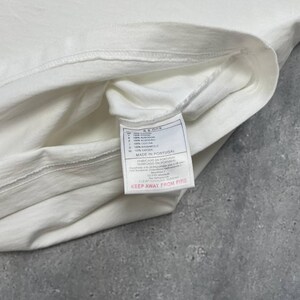 Peut inclure: Une tasse en c&eacute;ramique blanche avec une anse noire et le texte "But First, Coffee" en gras noir. La tasse est pos&eacute;e sur un fond flou, soulignant son design &eacute;pur&eacute;.