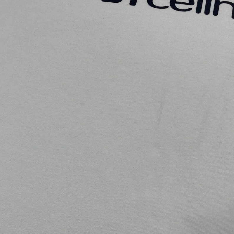 Pode incluir: Camiseta branca com a palavra "cellin" impressa em azul marinho na parte superior. O tecido parece ser um algod&atilde;o macio ou uma mistura de algod&atilde;o. A camiseta &eacute; lisa, sem outros elementos de design vis&iacute;veis.