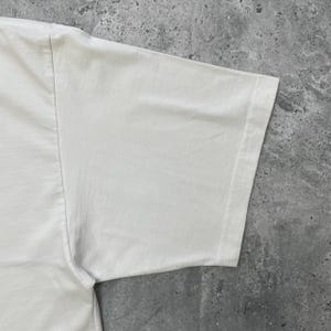 Peut inclure: Une tasse en c&eacute;ramique blanche avec une anse noire et le texte "But First, Coffee" en gras noir. La tasse est pos&eacute;e sur une surface en bois. La tasse mesure environ 10 cm de haut.