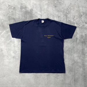 Op de afbeelding: Marineblauw T-shirt met korte mouwen. De voorkant van het shirt heeft de gouden tekst "We are Workstations apollo". Het t-shirt is gemaakt van een zacht materiaal en is waarschijnlijk vintage.