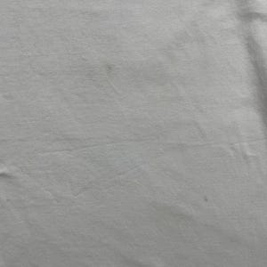 May include: Close-up of a white fabric with subtle variations in tone and texture. The material appears to be slightly wrinkled, with a few small, darker spots scattered across the surface. The overall impression is of a soft, plain textile.