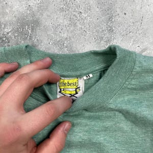 Pu&ograve; includere: T-shirt verde chiaro con scollo tondo. L'etichetta recita "the best" con un design giallo e nero. La maglietta &egrave; di taglia media.