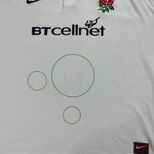 Pode incluir: Uma caneca de cer&acirc;mica branca com uma al&ccedil;a preta e o texto "But First, Coffee" em preto, em negrito. A caneca est&aacute; sobre uma superf&iacute;cie branca.