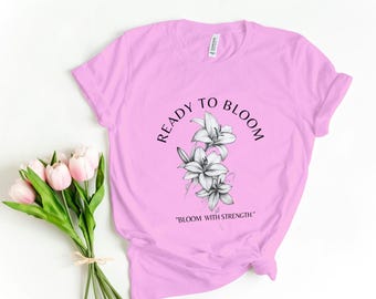 May include: Pink t-shirt with a black and white graphic of lilies and the text "Ready to Bloom" and "Bloom with Strength".