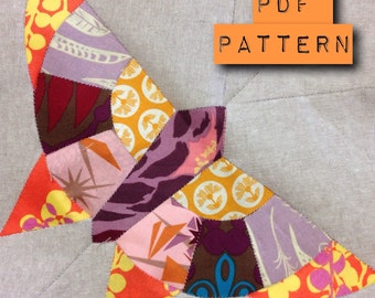 May include: A butterfly-shaped quilt block made of various fabric scraps in orange, yellow, purple, and brown with floral and geometric prints. The block is stitched onto a light beige fabric background. The text PDF PATTERN is visible.