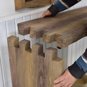 Puede incluir: Dos tablas de madera sin terminar con ensambles de dedos entrelazados. Una persona sostiene las tablas, mostrando la unión. La madera tiene una veta natural y un color marrón cálido, lo que sugiere un componente de mueble.