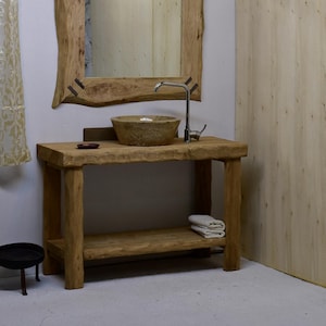 May include: A wooden vanity unit with a stone basin and chrome tap. The unit has a lower shelf and a matching wooden framed mirror. Two folded white towels are on the shelf. The vanity is made of natural wood.