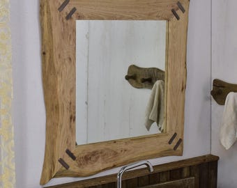Op de afbeelding: Een rustieke houten spiegel met een natuurlijke randlijst en metalen accenten. De spiegel is rechthoekig en heeft een vierkante reflectie. De lijst is gemaakt van lichtbruin hout met een natuurlijke afwerking. De spiegel hangt aan een witte muur boven een wastafel.