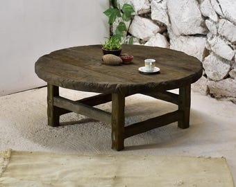 May include: A round, rustic wooden coffee table with a dark brown finish. The table has a thick, textured top and sturdy legs. A small potted plant, a bowl of berries, and a cup of coffee sit on the table. The table is approximately 40 inches in diameter.