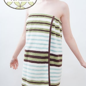 Puede incluir: Una envoltura de toalla a rayas en tonos blancos, verdes, marrones y azules. La envoltura se asegura con una banda marrón. La imagen incluye el texto "BlissfulPatterns PDF Pattern" en un gráfico ovalado.