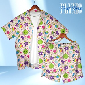 Könnte beinhalten: Ein zweiteiliges Pyjama-Set mit hellbeigem Hintergrund und einem farbenfrohen Muster aus Cartoon-Früchten, Sternen, Regenbogen und Edelsteinen. Das Set umfasst ein kurzärmeliges Hemd und passende Shorts, beide auf Holzbügeln.