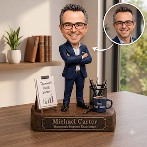Puede incluir: Una figura cabezona personalizada de un hombre con traje azul marino y gafas, sobre una base de madera con la inscripción Michael Carter Teamwork Inspires Excellence. Incluye una pizarra en miniatura con Teamwork Builds Success y una taza Best Team Leader.