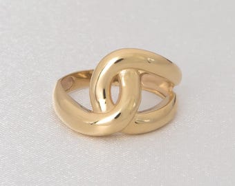 Puede incluir: Un anillo dorado con un diseño entrelazado. El anillo tiene una superficie lisa y pulida y un estilo simple y elegante. El anillo probablemente está hecho de oro o un metal dorado.