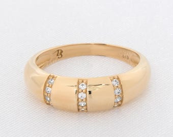 Puede incluir: Un anillo de oro con una banda redondeada. El anillo presenta tres secciones rectangulares, cada una adornada con pequeñas piedras preciosas transparentes. El anillo tiene un acabado pulido y está sobre un fondo blanco.