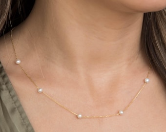Puede incluir: Un collar de cadena dorada delicada con cinco pequeñas perlas blancas espaciadas uniformemente. Los eslabones dorados, finos y pulidos, conectan cada perla individual, creando un aspecto refinado que descansa con gracia alrededor del cuello.