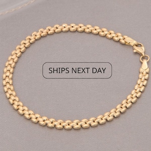 Op de afbeelding: Goudkleurige armband met een getextureerd, geschakeld ontwerp. De armband is gemaakt van een glanzend, metallic materiaal en heeft een sluiting. De tekst "SHIPS NEXT DAY" wordt weergegeven in een witte doos.