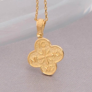 May include: A gold-colored pendant necklace featuring a four-leaf clover design. The pendant has a textured surface with a cross design in the center. The necklace chain is delicate and gold-toned, suitable for everyday wear.