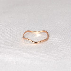 Puede incluir: Un anillo de oro rosa con una forma ondulada y org&aacute;nica. El anillo se presenta sobre un fondo blanco, resaltando su superficie lisa y pulida. El dise&ntilde;o minimalista del anillo lo convierte en una joya vers&aacute;til.