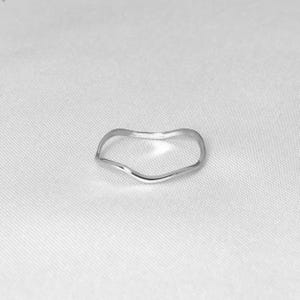 Puede incluir: Un anillo de plata minimalista con un dise&ntilde;o ondulado y org&aacute;nico. El anillo tiene un acabado liso y pulido y una forma delicada y fluida. El anillo est&aacute; sobre un fondo blanco.