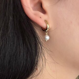 May include: Gold hoop earrings with a single white pearl dangling from the bottom.