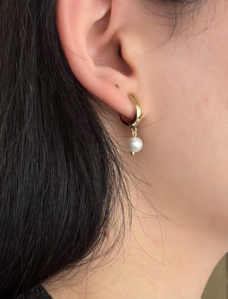 May include: Gold hoop earrings with a single white pearl dangling from the bottom.