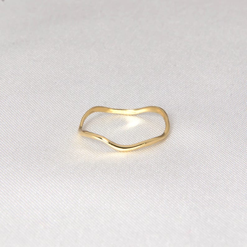 Puede incluir: Un delicado anillo de oro con un dise&ntilde;o ondulado y org&aacute;nico. La superficie lisa y pulida del anillo refleja la luz, creando un brillo sutil. El estilo minimalista lo convierte en un accesorio vers&aacute;til para el uso diario. El anillo es una joya sencilla pero elegante.