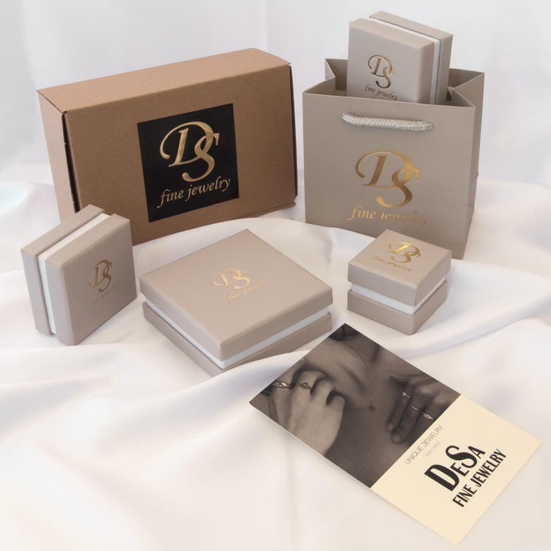 May include: A brown box with a gold logo that says "Desa Fine Jewelry" and a smaller white box with a gold logo that says "Desa Fine Jewelry". There is also a white paper bag with a gold logo that says "Desa Fine Jewelry".