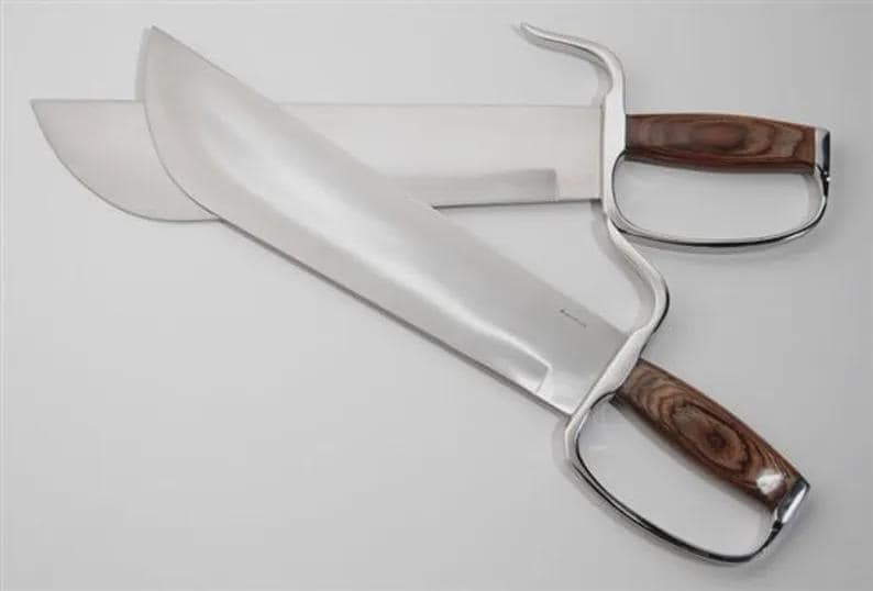 May include: Two stainless steel butterfly swords with wooden handles. The blades are wide and curved, with a polished finish. The handles have a finger loop design. The swords are displayed on a white surface.
