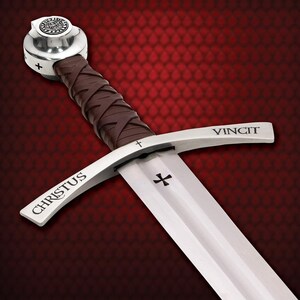 May include: A medieval sword with a silver blade and guard, featuring the inscription "CHRISTUS" and "VINCIT". The handle is wrapped in brown leather. The pommel is silver with a circular emblem and a cross.