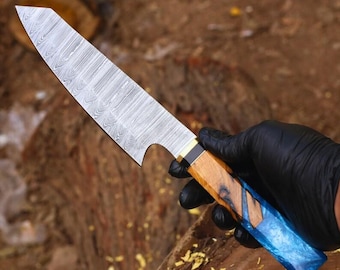 May include: A Damascus steel chef's knife with a patterned blade. The handle is a combination of wood and blue resin, accented with brass. The knife is designed for kitchen use.
