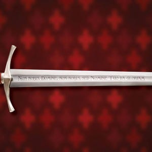 May include: A silver sword with a cross-shaped hilt and a long, engraved blade. The blade features the inscription "Non Nobis, Domine, Non Nobis, Sed Nomine Tuo Da Gloriam" in a serif font. The background is a dark red with a repeating pattern.