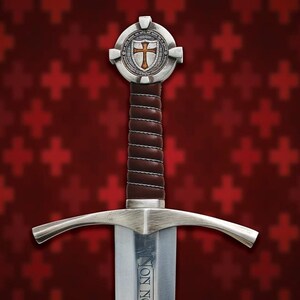 May include: A medieval sword with a silver blade and guard, featuring a brown leather-wrapped handle. The hilt has a circular emblem with a cross design. The background is a pattern of red crosses.